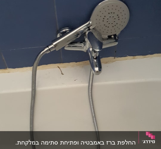 ברז מקלחת עם צינור ומזלף על קיר כחול